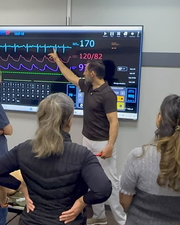Instrutor da Pulso Academy explicando ritmos cardíacos no monitor de simulação para um grupo de profissionais da saúde