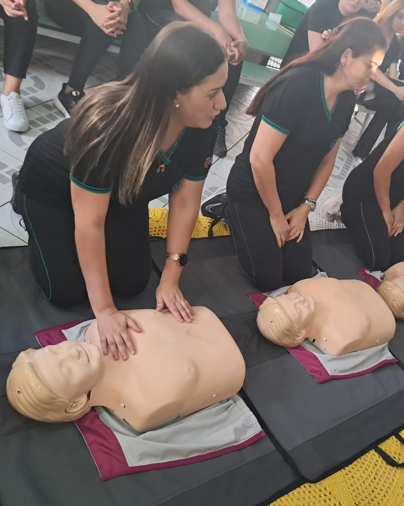 Equipe de uma escola praticando massagem cardíaca em manequins durante treinamento da Pulso